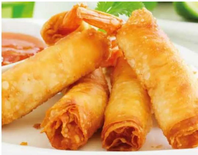Close-up of golden-brown rolled food rolls on a white plate, garnished with parsley.