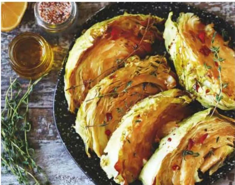 Close-up of sliced cabbage rolls with sauce and herbs, served on a dark plate with herbs and spices in the background.
