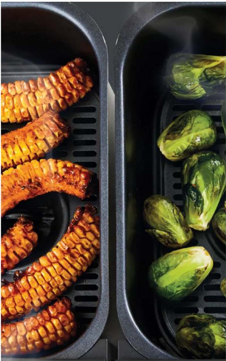 Two black electric fans containing cooked corn cobs and bok choy, placed on a steamer (no text or symbols visible)