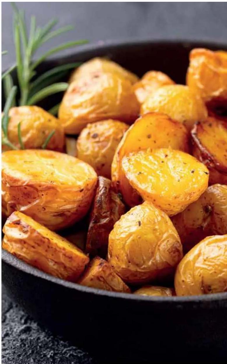 Close-up of golden-brown baked potatoes in a black bowl, garnished with green rose and olive oil (no text or symbols visible)
