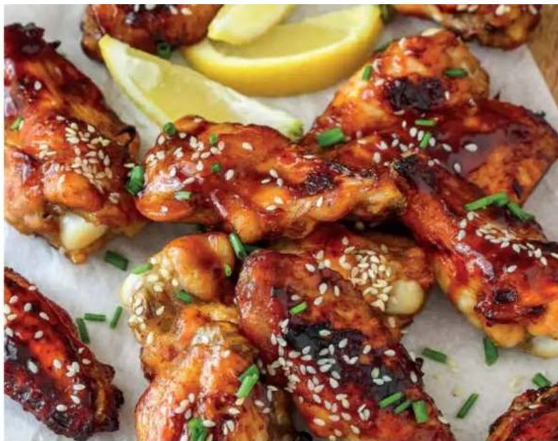 Close-up of glossy braised chicken wings garnished with sesame seeds and green onions, served on a white plate with lemon slices (no text or symbols visible)