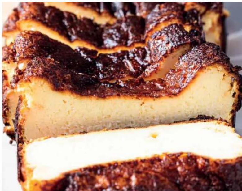 Close-up of a baked pastry with dark brown topping and white cream, showing layered crust and sliced pieces (no text or symbols visible)