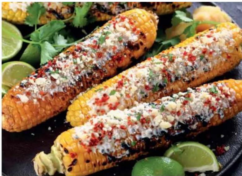 Close-up of three freshly baked corn cobs topped with chopped garlic, chili, and lime, garnished with cilantro (no text or symbols visible)