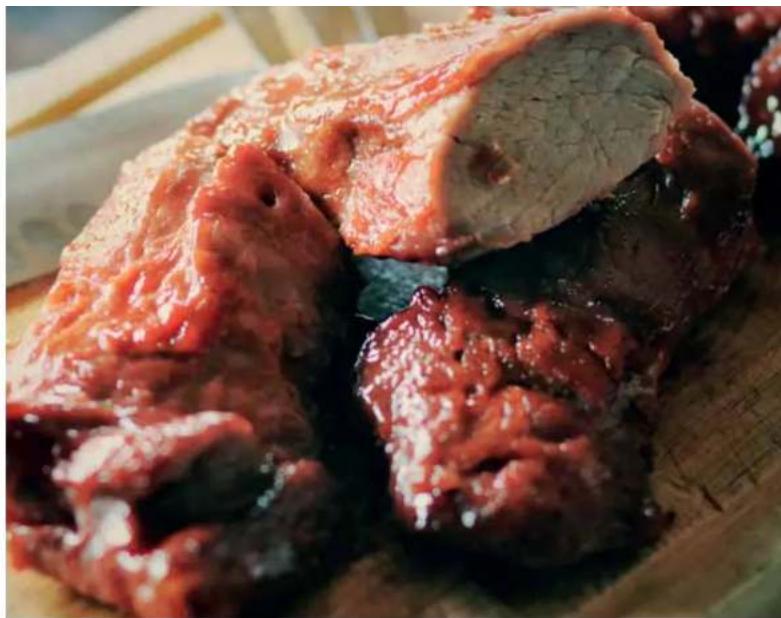 Close-up of a cooked meat dish with glossy sauce and visible chunks, served on a wooden cutting board (no text or symbols)