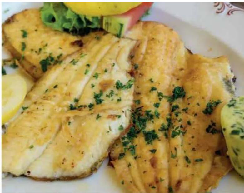 Plated dish of golden fish fillets garnished with parsley and lemon slices (no text or symbols visible)