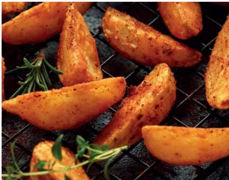 Close-up of golden-brown baked potatoes on a metal grater with fresh herbs (no text or symbols visible)