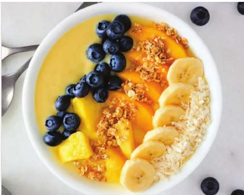 Top-down view of a bowl of smooth blueberries and sliced bananas with craniums, presented on a white surface with scattered blueberries (no text or symbols visible)
