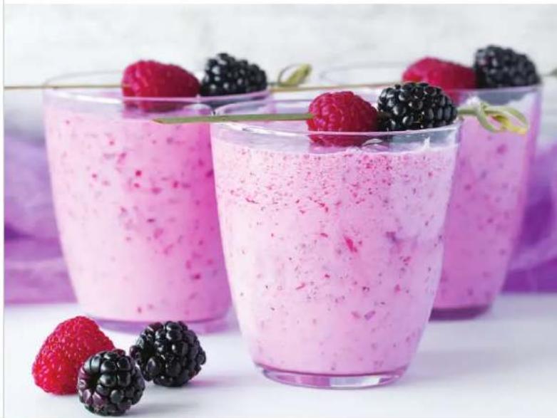 Three glasses of pink smoothie with berries and a green leaf, surrounded by fresh strawberries (no text or symbols visible)