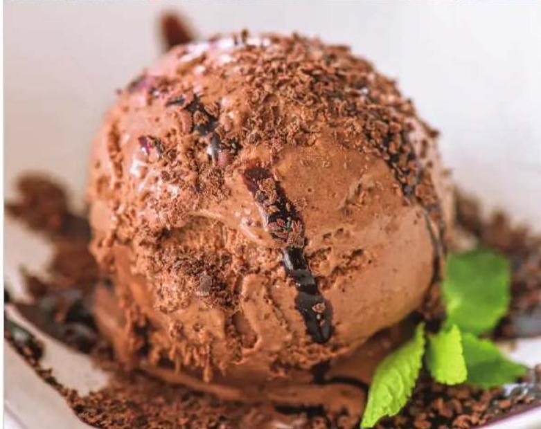 Close-up of a chocolate ice cream with powdered sugar and mint leaves, served on a white plate (no text or symbols visible)