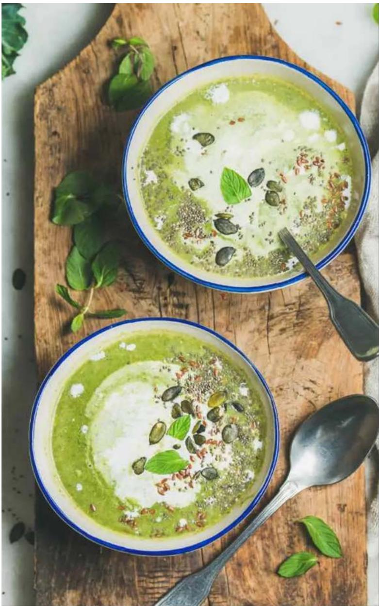 Two bowls of green creamy soup garnished with small green leaves and herbs, served on a wooden cutting board (no text or symbols visible)