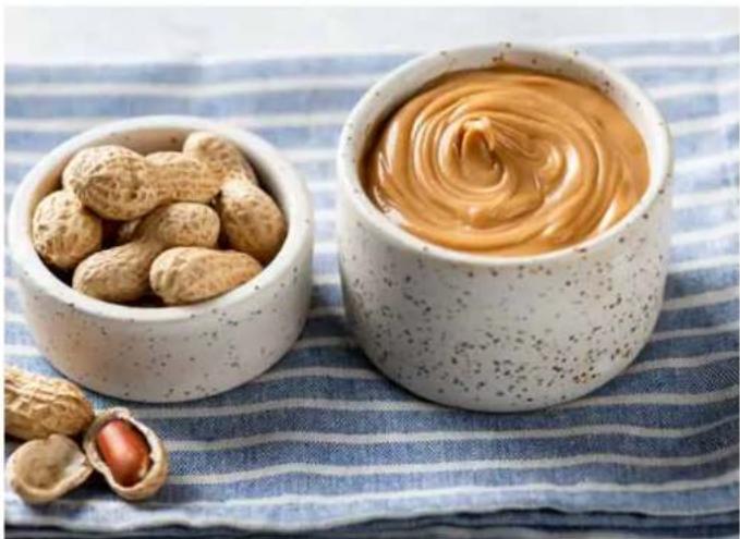 Two bowls of peanuts: one filled with nuts, the other with a swirling orange sauce, placed on a blue striped cloth (no text or symbols visible)
