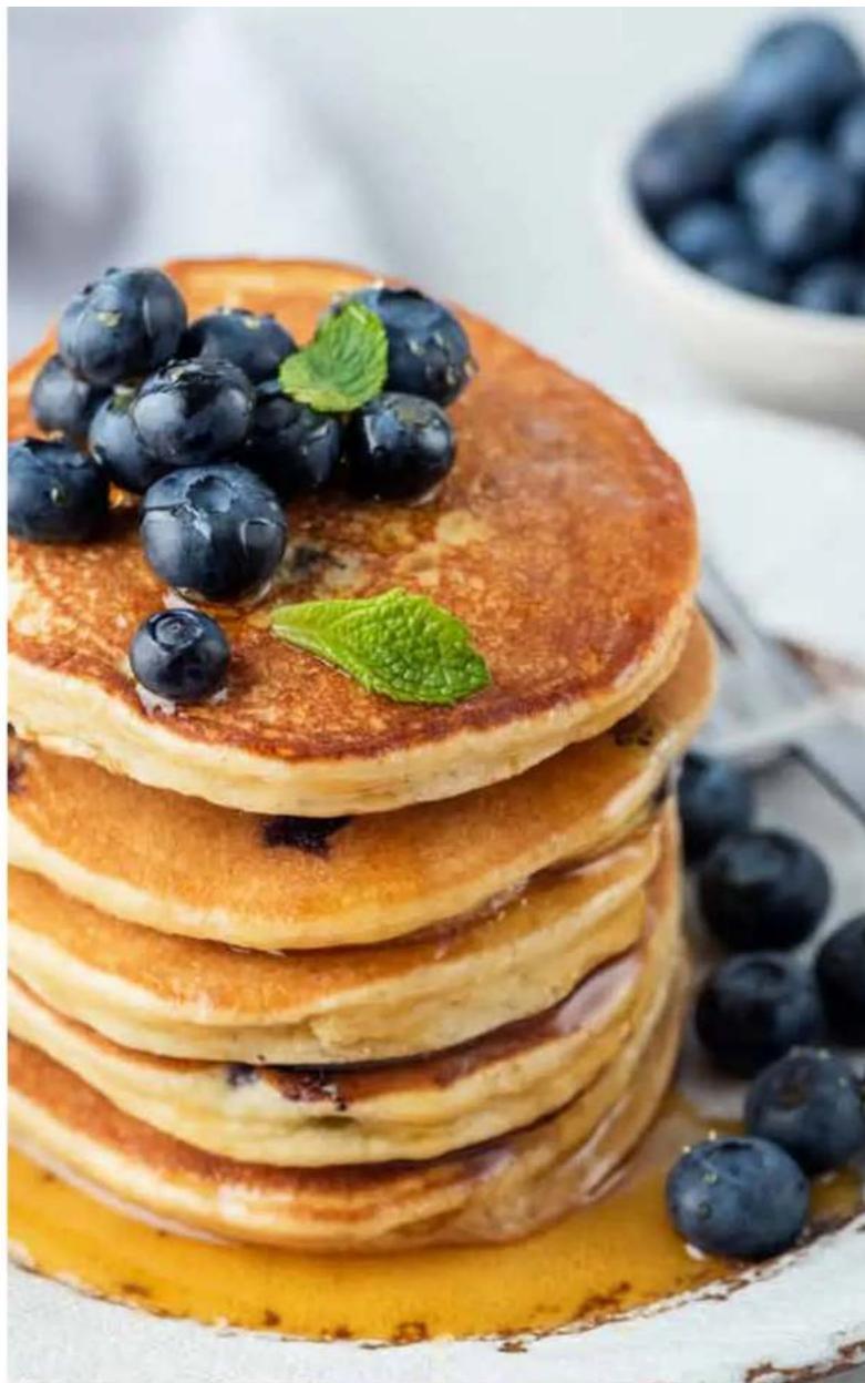 Stack of blueberries topped with fresh blueberries and mint leaves, served on a plate with blurred blueberries in the background (no text or symbols visible)