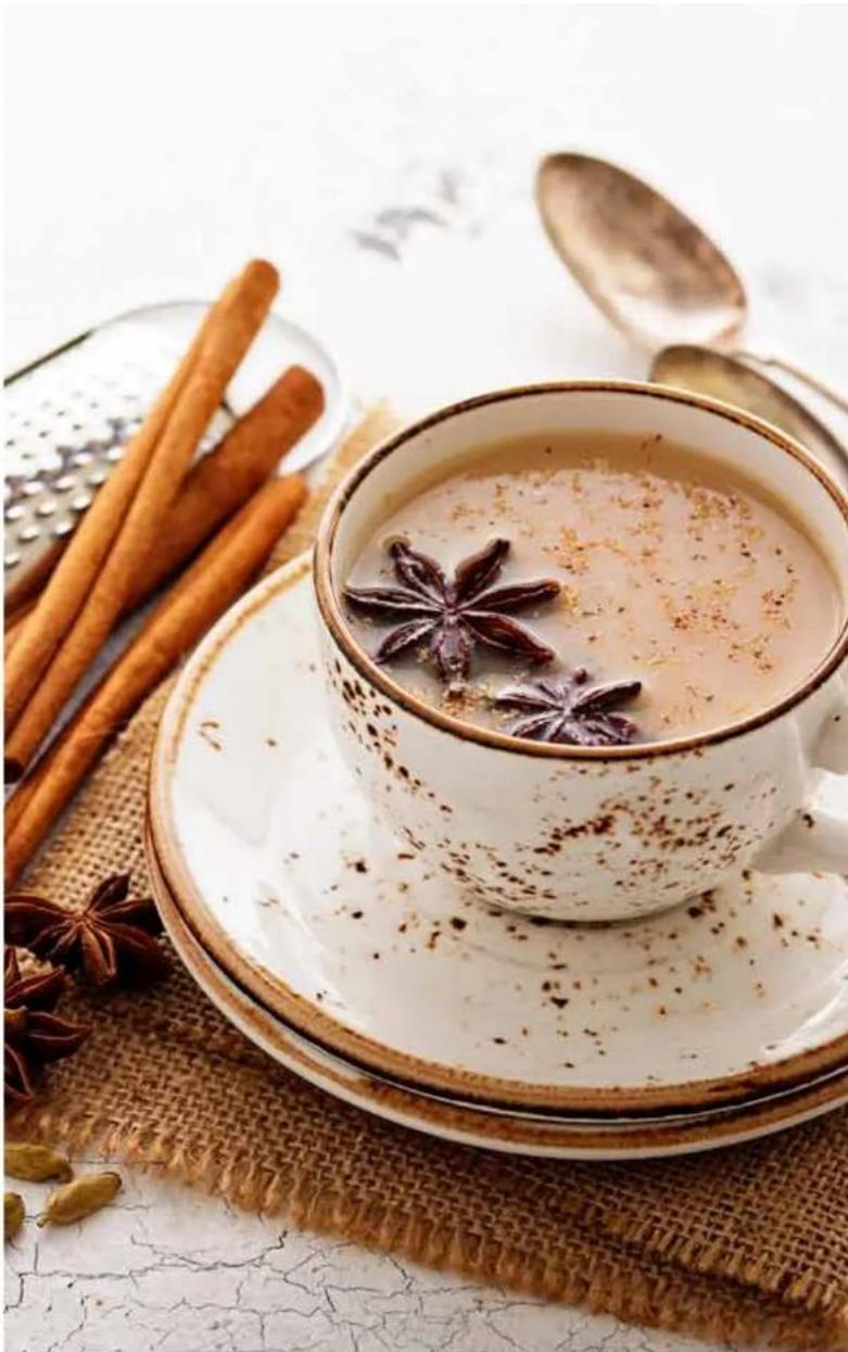 A teacup filled with star anise, accompanied by cinnamon sticks and a spoon on a woven mat (no text or symbols visible)