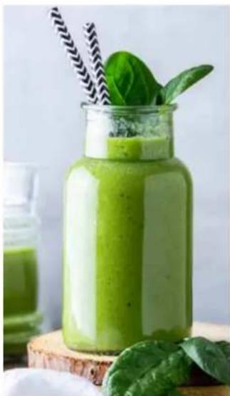 Green smoothie in a glass jar with leafy greens and straw, accompanied by fresh spinach leaves on a wooden surface (no text or symbols visible)