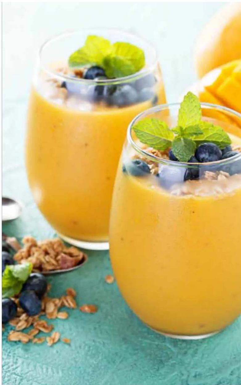 Three glasses of orange smoothie with blueberries and mint leaves, surrounded by fresh fruits and nuts on a teal surface (no text or symbols visible)