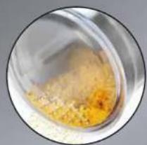 Close-up of a glass container containing a yellowish granular substance, possibly food or salt, with no visible text or symbols.