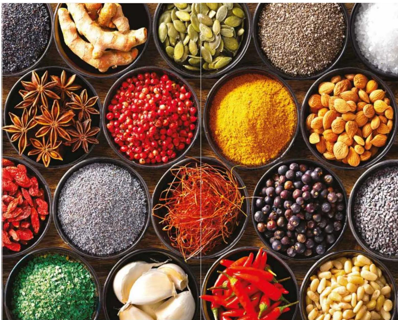 Overhead view of various spices and herbs in black bowls arranged on a wooden surface (no text or labels visible)