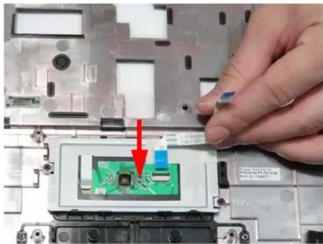 Close-up of a hand pressing a green circuit board component on a laptop motherboard, with a red arrow indicating the component's direction (no text or symbols visible).