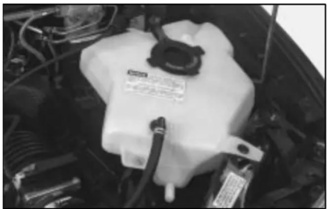 Close-up of a white plastic automotive engine compartment with visible hoses and components (no text or symbols)