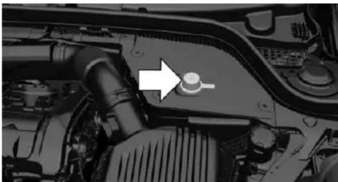 Close-up of a car engine bay with a white arrow pointing to a component on the top (no visible text or symbols)