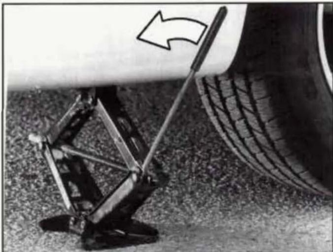 Close-up of a mechanical suspension device on grass next to a tire, with an arrow indicating direction (no text or symbols)