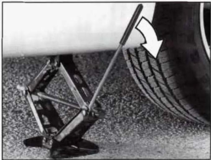 Close-up of a car tire being adjusted with a lever, showing tire tread pattern and motion direction (no text or symbols)