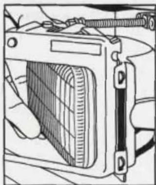 Illustration of a hand holding a rectangular device with a grid pattern, attached to a wall-mounted bracket (no text or symbols visible)