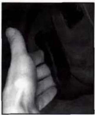 Close-up of a human hand resting on a dark surface, possibly part of a vehicle or mechanical component (no visible text or symbols)