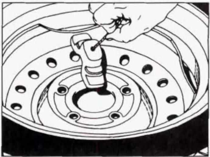 Illustration of a hand using a tool to adjust or install a car tire component (no text or symbols visible)