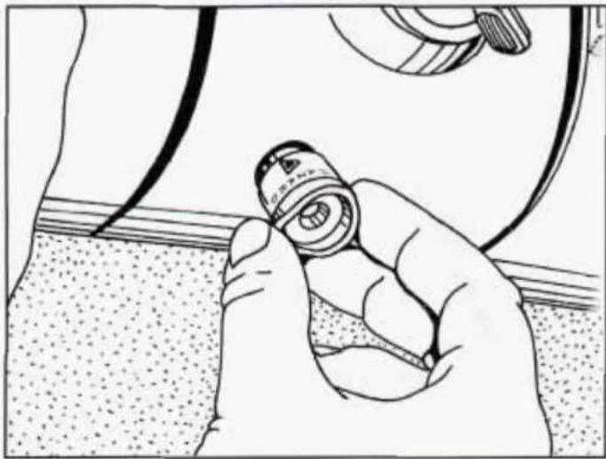 Illustration of a hand holding a small mechanical component, with no visible text or symbols