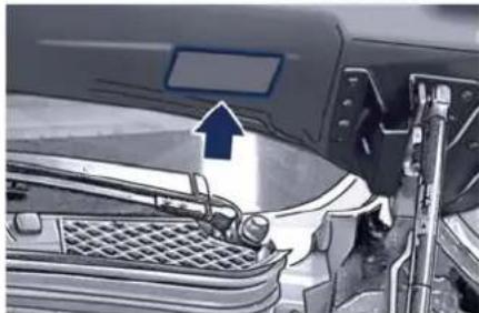 Close-up of a car engine compartment with a blue arrow pointing to the hood (no visible text or symbols)