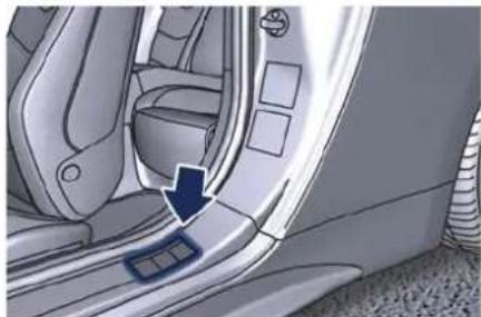 Interior view of a car showing the side panel and seat area with an arrow pointing to a small component (no text or symbols visible)