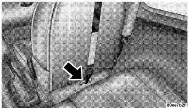 Close-up of a car seatbelt with a black arrow pointing to the side panel (no text or symbols visible)