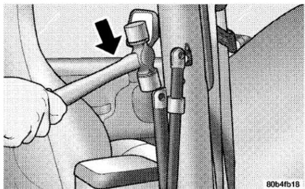 Mechanical assembly diagram showing a hand adjusting a seatbelt with a black arrow indicating the direction (no text or symbols present)