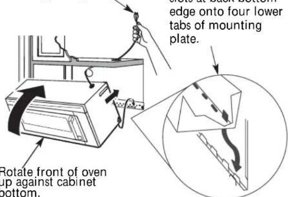 Rotate front of oven up against cabinet bottom. Rotate at back bottom edge onto four lower tabs of mounting plate.