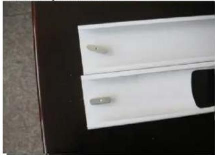 Close-up of a white plastic panel with two small metallic components, placed on a dark surface (no text or symbols visible)