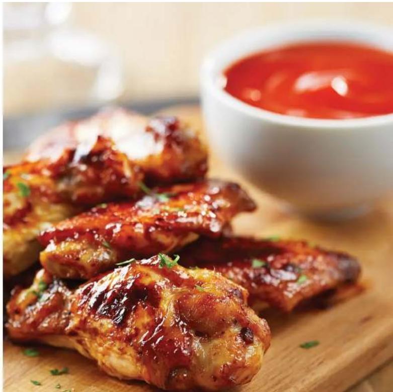 Close-up of braised chicken wings garnished with green herbs, served on a wooden cutting board with a red sauce bowl in the background (no text or symbols visible)