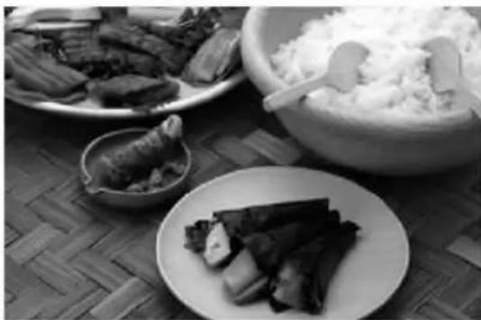 Black-and-white photo of a plated dish featuring sliced meat, rice, and a bowl of rice on a woven mat (no text or symbols visible)