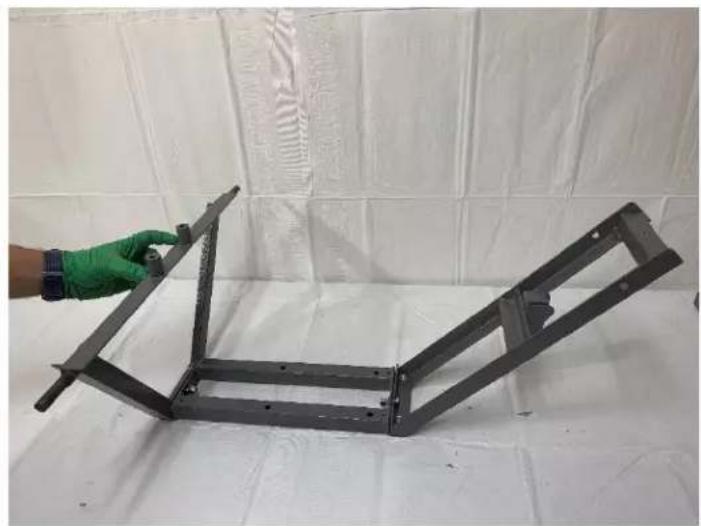 Hand holding a metal frame with a green glove, against a white tiled wall (no text or symbols visible)