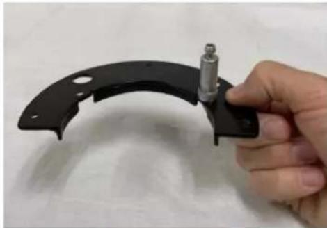 Hand holding a black plastic mechanical bracket with a metal screw, against a plain white background (no text or symbols visible)