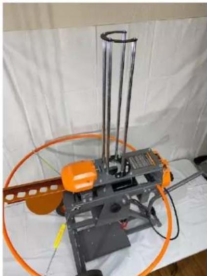 Industrial robotic device with orange components and metal frame, displayed on white fabric (no visible text or symbols)