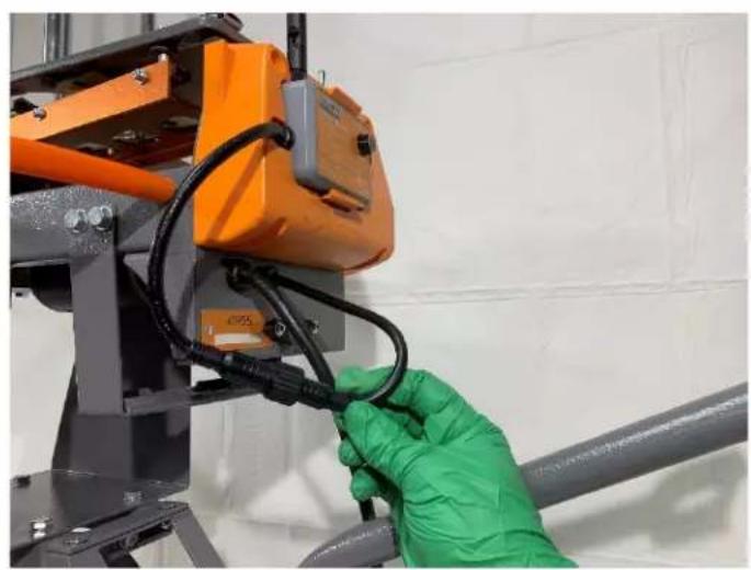 Close-up of a gloved hand installing or adjusting cable on an orange industrial machine component (no visible text or symbols)