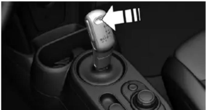 Close-up of a car gear shift lever with a white arrow pointing to the left side (no text or symbols visible)