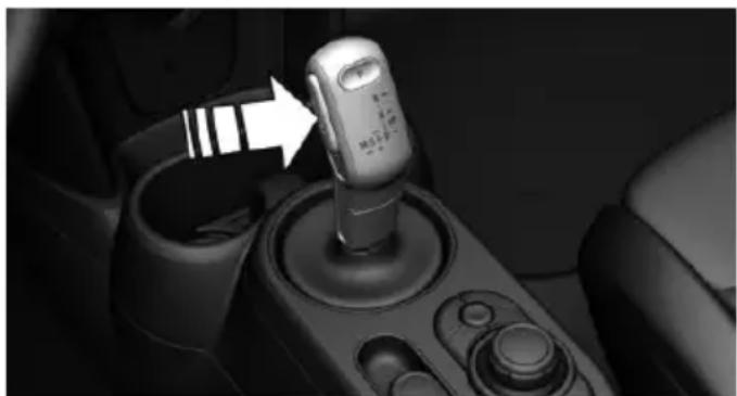 Close-up of a car gear shift lever with a white arrow pointing to the mode (no visible text or symbols)