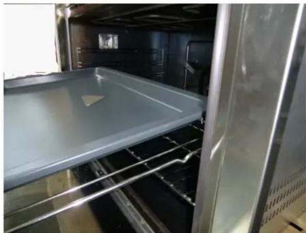 Interior view of a stainless steel oven with a tray placed inside, showing metal grilles and ventilation ducts (no text or symbols visible)