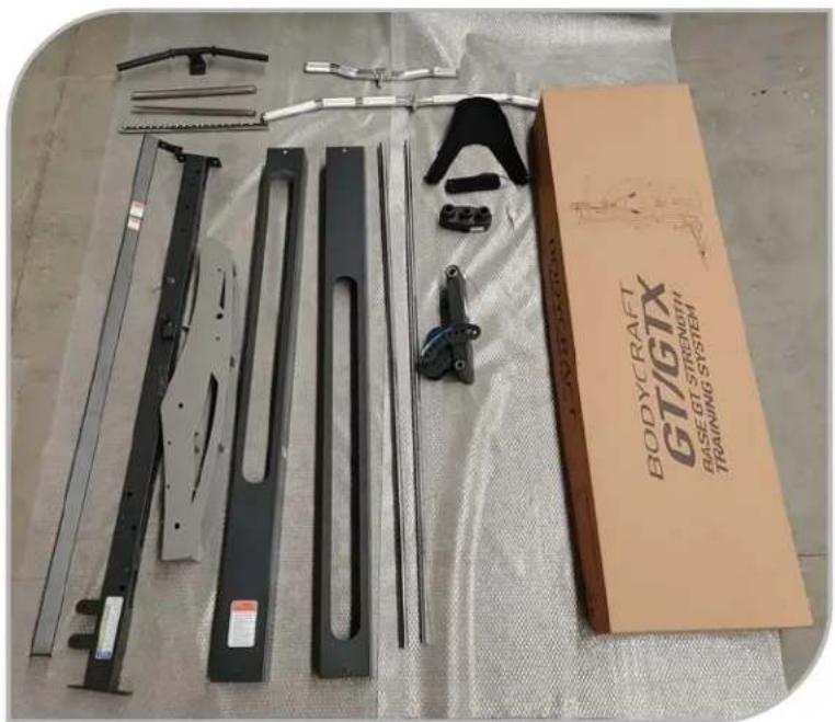 Assorted mechanical components laid out on a cloth, including metal brackets, crimping tools, and a BodyCRAFT GTIGTX Training System box (no visible text or symbols on parts)