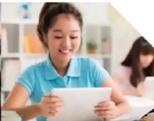Young girl in blue shirt using tablet in classroom setting (no visible text or symbols)