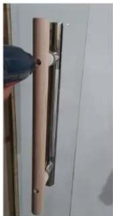 Close-up of a metallic door handle with a hand holding a blue clip (no text or symbols visible)