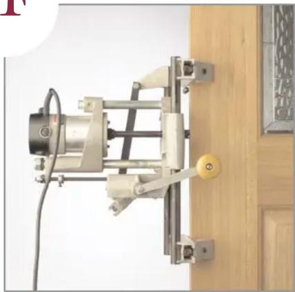 Mechanical device mounted on a wooden door, showing mechanical components and wiring (no visible text or symbols)