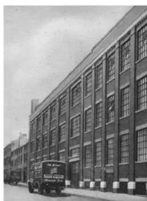 Exterior view of a multi-story industrial building with a vintage truck parked in front (no visible text or signage)
